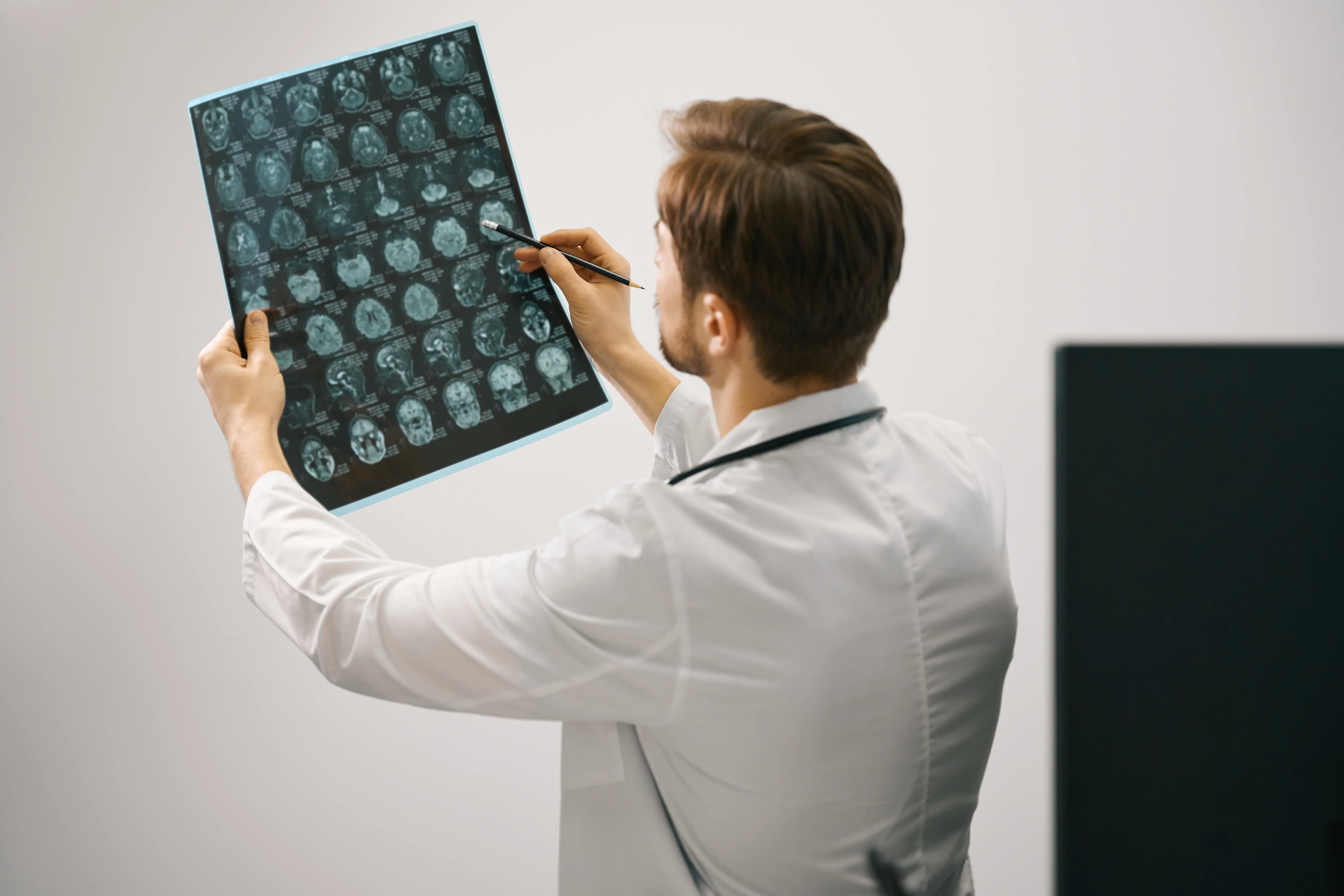 A consultant radiologist examining brain MRI scans with a pencil, marking regions of interest.